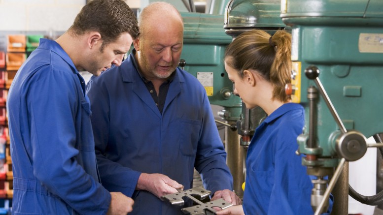 Three machinists in workspace by machine talking