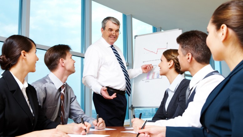 Elderly boss pointing at whiteboard and looking at managers during presentation