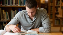 Male student researching with a book in a library