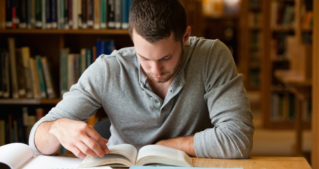 Male student researching with a book in a library