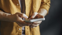 Happy Asian Man in a Yellow Shirt Using a Smartphone to Check Social Media