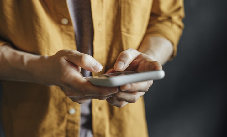 Happy Asian Man in a Yellow Shirt Using a Smartphone to Check Social Media