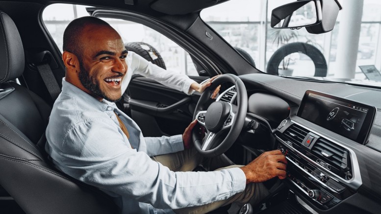 Young african american man sitting in a new car in car showroom and looking around