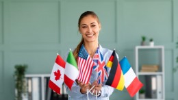Happy female tutor showing bunch of diverse flags, recommending foreign language studying school