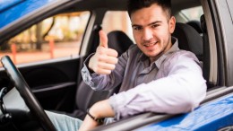 Happy smiling man sitting inside car showing thumbs up. Handsome guy excited about his new vehicle. Positive face expression