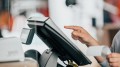 Young saleswoman doing process payment on the touchscreen POS, counting sale in the cash register, finance concept