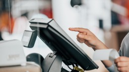 Young saleswoman doing process payment on the touchscreen POS, counting sale in the cash register, finance concept