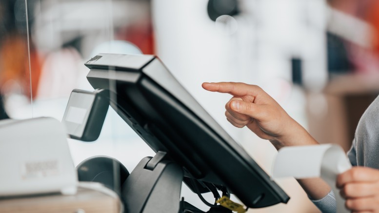 Young saleswoman doing process payment on the touchscreen POS, counting sale in the cash register, finance concept